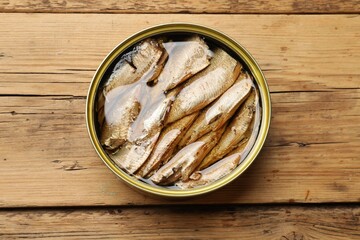 Tasty sprats in tin can on wooden table, top view