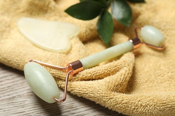 Face roller, gua sha tool, towel ruscus branch on wooden background, closeup