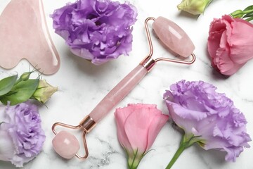 Face roller, gua sha tool and beautiful flowers on white marble background, flat lay