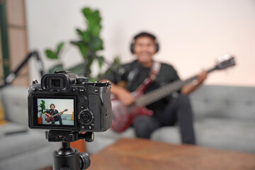 Bassist or guitarist blogger. Asian influencer playing bass, recording music videos using a professional camera on a tripod. Bassist creates video lessons and tutorials for internet vlog classes.