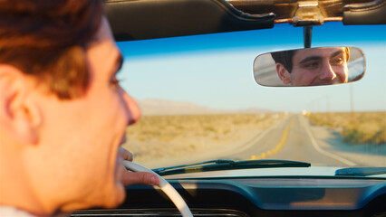 Naklejka premium Male Driver Reflected In Mirror Driving Classic Open Top Car On Road Trip Through Countryside