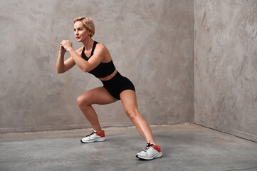 Athletic woman stretching her leg while warming up for sports training. The girl coach performs a side lunge. European woman in black shorts and top is exercising.