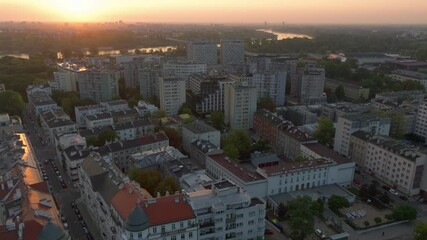Aerial views capture the sun bathing a Warsaw residential area in warm light. Cars navigate the streets below, emphasizing the lively urban scene during golden hour