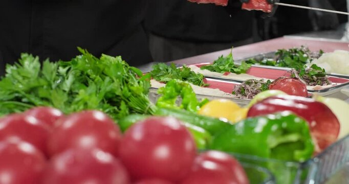 Chef serving plate for Turkish kebab, takes grilled tomatoes from skewer. Traditional Turkish kebab served with flat bread, parsley and vegetables. Arabic food