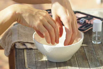Preparing for a classic trim manicure: a woman holds her fingers in a bowl of hot water, close-up photo. A girl takes care of her nails at home. Regular procedures for beautiful looking hands.