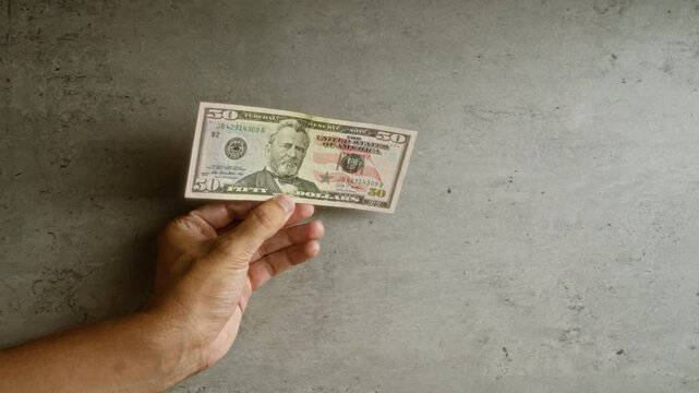 Hand holding american fifty-dollar bill against a concrete background, highlighting the concept of currency and finance in the united states.