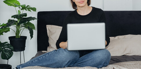 Young woman working on a laptop while seated on a bed in a cozy room