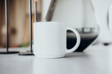 A simple white mug on a kitchen countertop beside a coffee maker