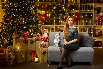 A beautiful woman is waiting for guests in the living room near the Christmas tree for a festive...