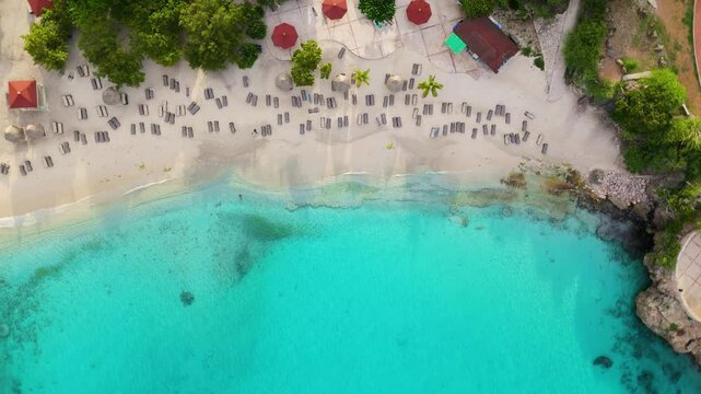 Top-down speed ramp rising and orbiting above Grote Knip or Playa Abou in Curacao, showing clear turquoise waters, sandy shore, and vibrant green surroundings