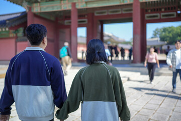 A Korean couple, a man in his 30s and a woman in her 20s, walks harmoniously through a historical building in Seoul, South Korea, wearing Hanbok.