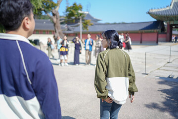 A Korean couple, a man in his 30s and a woman in her 20s, walks harmoniously through a historical building in Seoul, South Korea, wearing Hanbok.