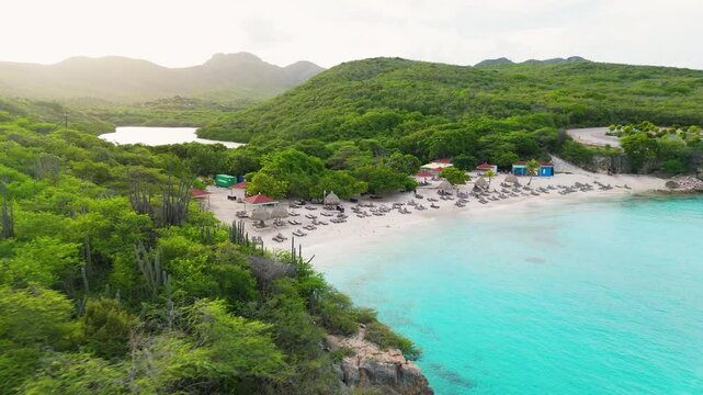 Aerial establishing view of Grote Knip in Curacao, showcasing turquoise waters, sandy shore, and island greenery with beach chairs spread across sand
