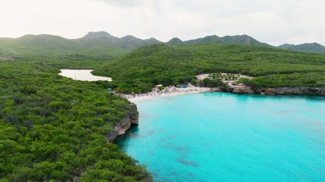 Drone panoramic overview of the coastline at Kenepa Grande , Curacao, with clear turquoise waters, lush green surroundings, and sandy beach shoreline