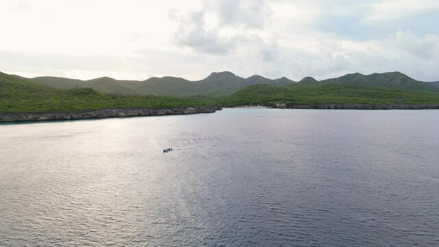 Aerial drone establishing overview of peaceful tropical bay at Kenepa Grande , capturing lush green hills surrounding the calm turquoise waters of the Caribbean