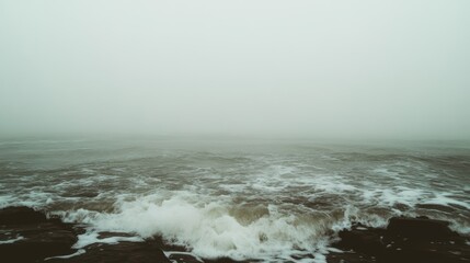 Waves surge against rocks as fog envelops the ocean, creating a dramatic and moody coastal landscape