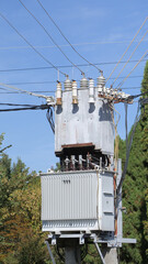 An electrical distribution transformer on a pole, connected to numerous wires, set against a...