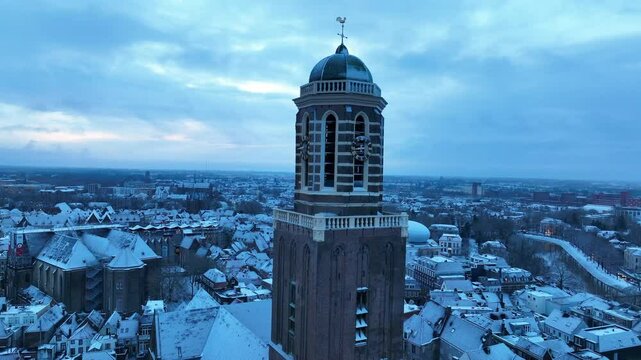Zwolle Peperbus church tower rising up over the snow covered rooftops in the downtown district aerial drone view during a cold winter sunrise.