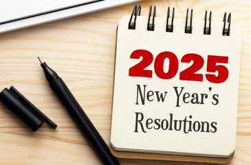 2025 New Year's Resolutions text in a notebook on a wooden desk.