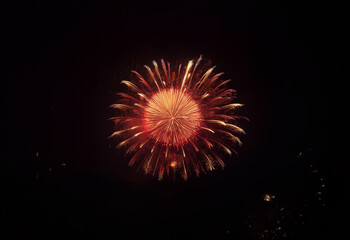 Fototapeta premium A single firework bursts in the night sky, radiating bright red and orange sparks against a dark, isolated background.