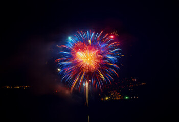 A single firework explodes in a burst of red, blue, and yellow against a black night sky.