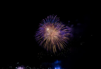 Fototapeta premium A single firework explodes in a burst of purple and gold against a dark, isolated background.
