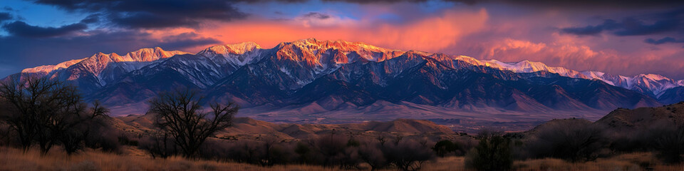 Fototapeta premium Panoramic view of a majestic mountain range at sunrise with glowing peaks and vibrant sky, nature landscape background