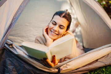 Young caucasian woman reading a book in her tent in backyard