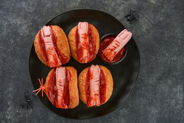 Halloween background. Homemade hot dogs with bloodied fingers on dark table for Halloween. Themed...