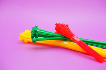 bundle of zip ties isolated on purple background. zip ties in red, green, and yellow colors arranged in a stacked manner. Cable ties or cable ties, straps that can be used for various purposes.