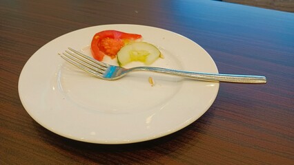 Empty plate with a fork, tomato and cucumber slices on a wooden table.