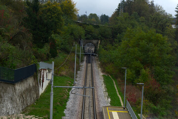 The image shows a railway track leading into a tunnel surrounded by lush greenery and trees. 