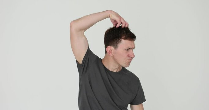 Man in black t-shirt scratches head playing monkey on white background. Funny male pretends to be animal with facial expression and gestures