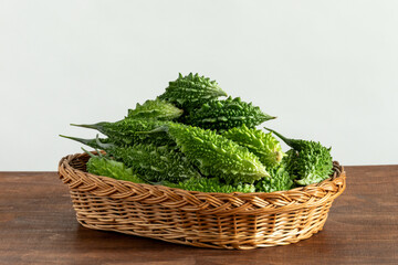 Freshly harvested organic bitter melons (Momordica charantia) in a wicker tray on wooden table....