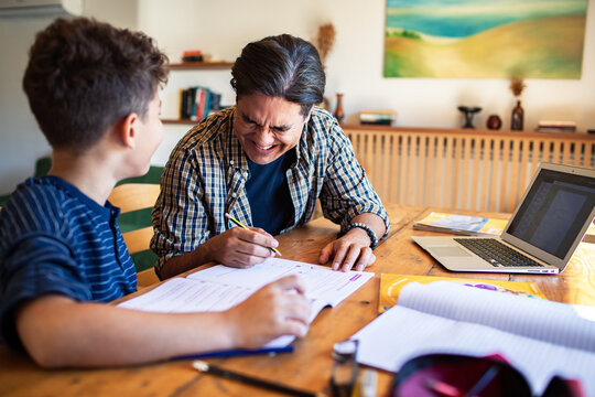 Father laughing while helping son with homework on desk