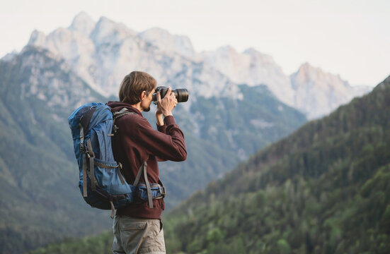 Young cheerful man photographer taking photographs with digital camera in mountains. Travel and active lifestyle concept