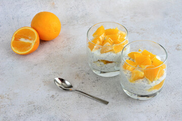 a glass of yogurt with chia and oranges and a spoon next to it