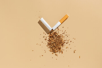 Broken cigarette with scattered tobacco on beige background. Smoking cessation and quitting concept. World no tobacco day.