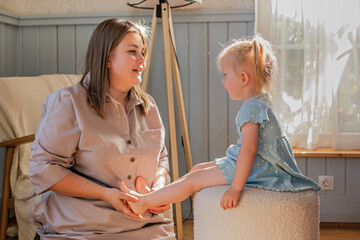 Mother plays with her little daughter and tickles her bare feet.