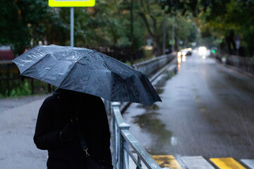 Portrait of a person holding black umbrella outside during the rain. Raindrops and light from city...