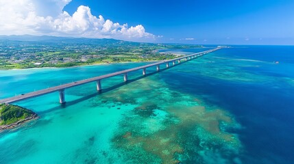 An aerial view of a long bridge connecting two islands, with turquoise water and a blue sky with white clouds.