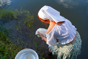 Beautiful young woman in nightie stands in the river and washes clothes.