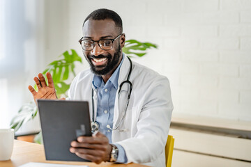 Smiling African-American doctor using a tablet for a virtual consultation, dressed in a white coat,...
