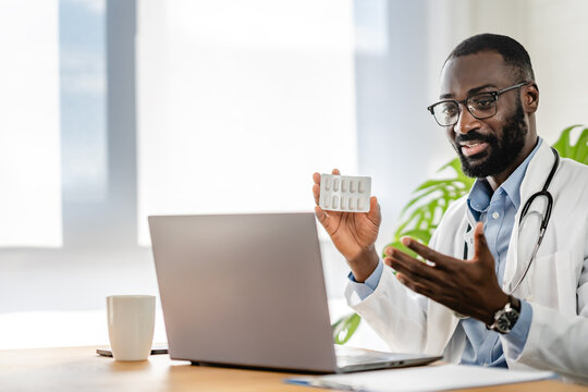 Smiling African-American doctor having an online consultation on his laptop in a bright, modern office. He appears engaged, communicating effectively with a patient.