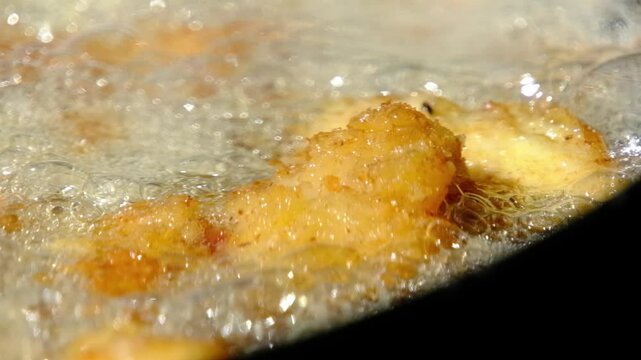 Slow motion and extreme close up while deep frying catfish nuggets or fish in batter and breadcrumbs in cast iron skillet or pan over firepit while camping outdoors