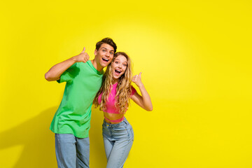 Portrait of two nice young partners show thumb up empty space wear t-shirt isolated on vibrant yellow color background