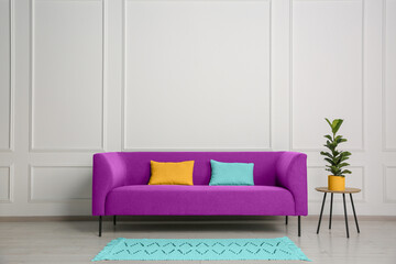 Stylish magenta color sofa, pillows and table near white wall indoors
