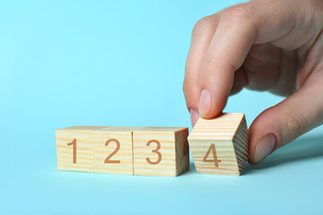Man putting wooden cube with digit 4 to row of other numbered ones on light blue background, closeup. Step-by-step concept