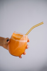 Refreshing orange smoothie served in a glass with a reusable straw on a plain background