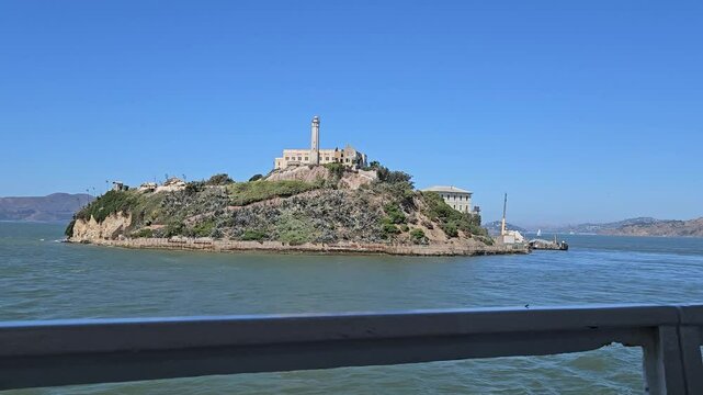 Alcatraz island and prison. View from a moving tourist boat, ferry. Former prison, Federal Penitentiary. Motion of sea waves and yachts in the background. San Francisco, California, United States